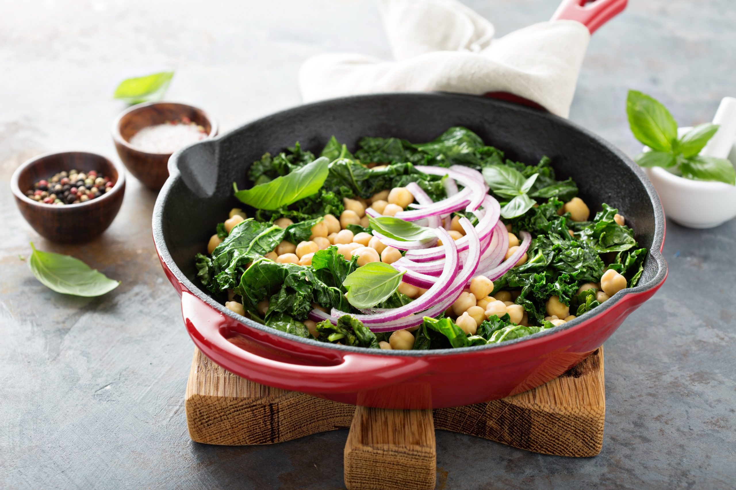 Chickpeas, kale, and onion in a skillet on a cutting board