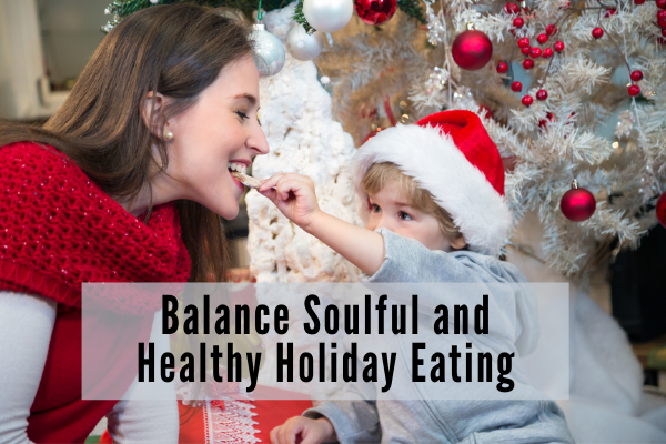 A woman and young child sit in front of a christmas tree. The child feeds to the woman a christmas cookie.