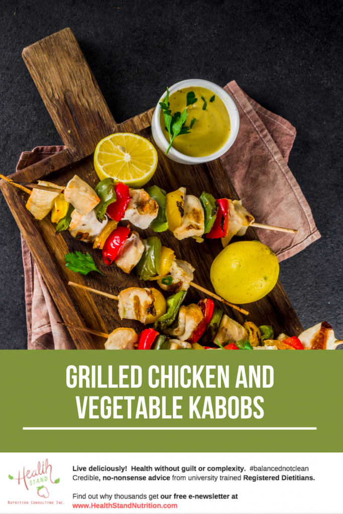 cooked chicken and vegetable kabobs displayed on a wooden cutting board along with lemon halves and a bowl of dipping sauce