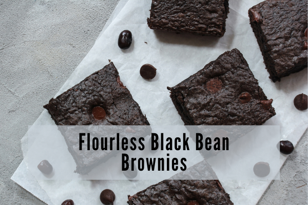 Squares of dark chocolate brownies arranged on a white plate with black beans scattered around them