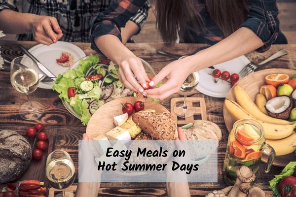 A group sharing an easy summer meal with salad, bread, fruit, cheese, and drinks at an outdoor table.