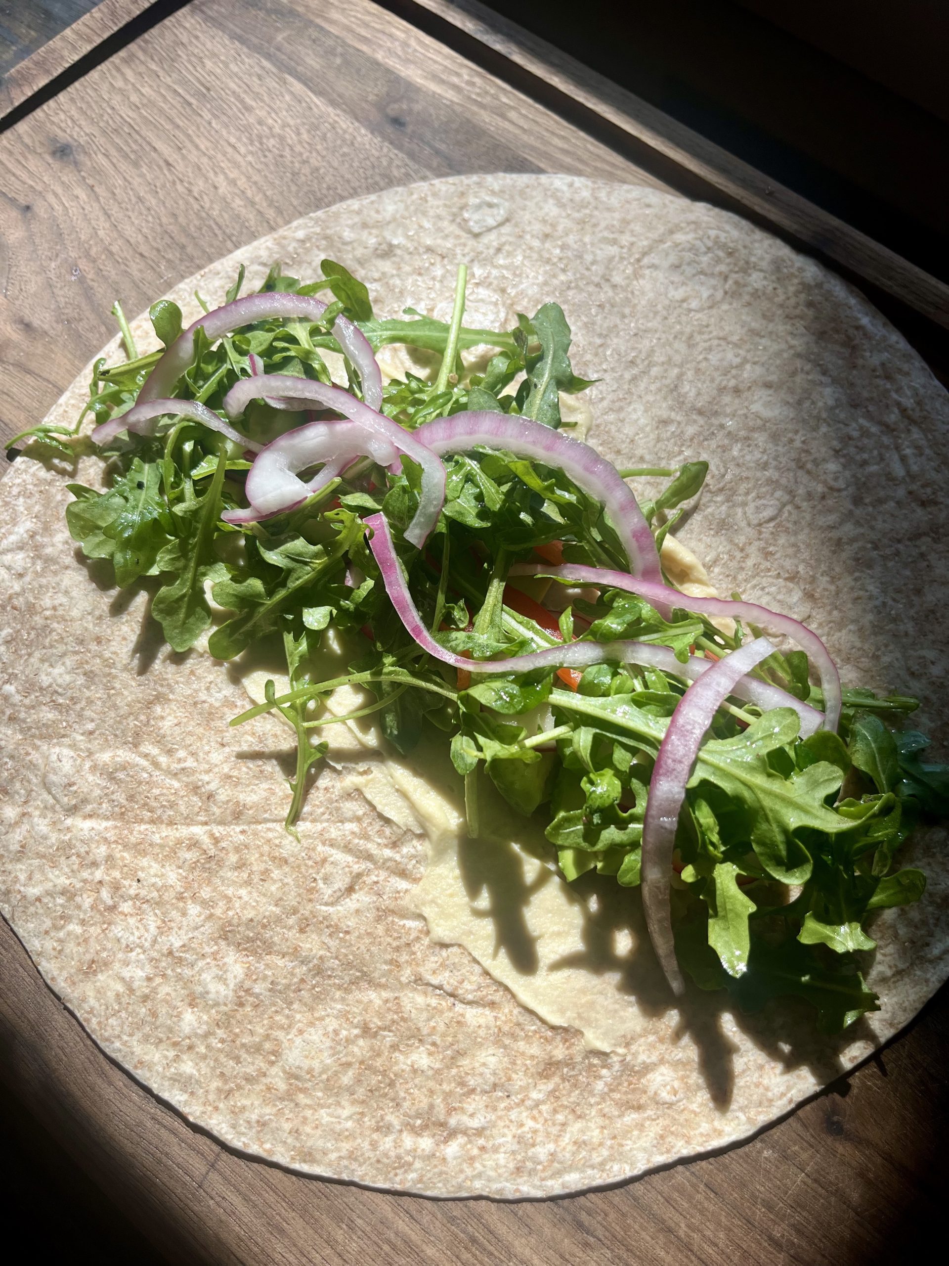 Loaded veggie and hummus wrap with cucumber, bell pepper, avocado, arugula, and red onion