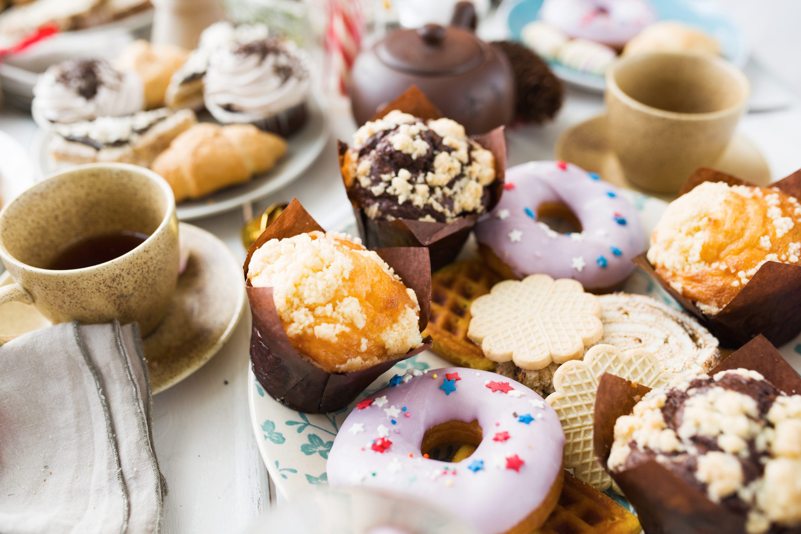 Fresh dessert Fresh donuts, cookies and muffins on served table with cups of tea near by to represent what people call sugar addiction