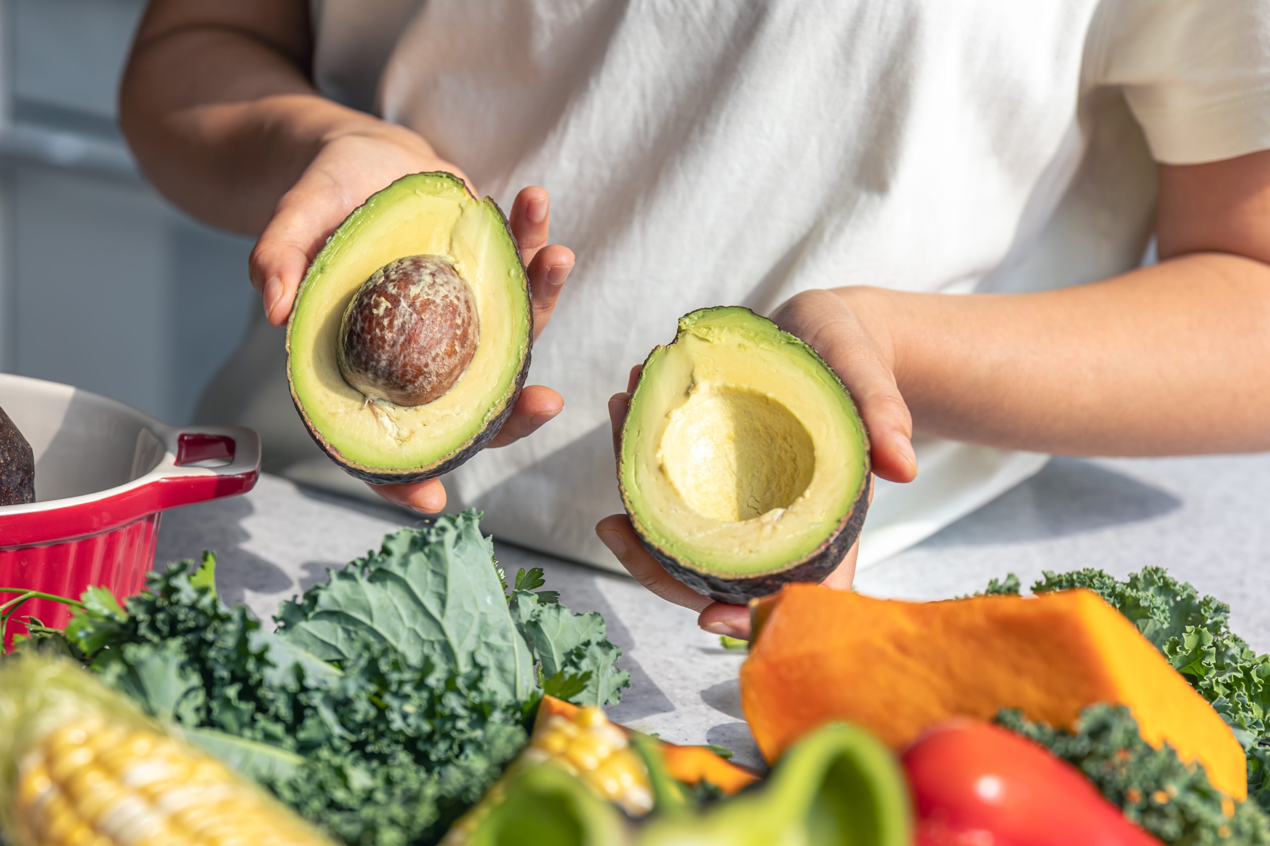 Avocado halves in a female hand in the kitchen. male and female athlete supporting each other