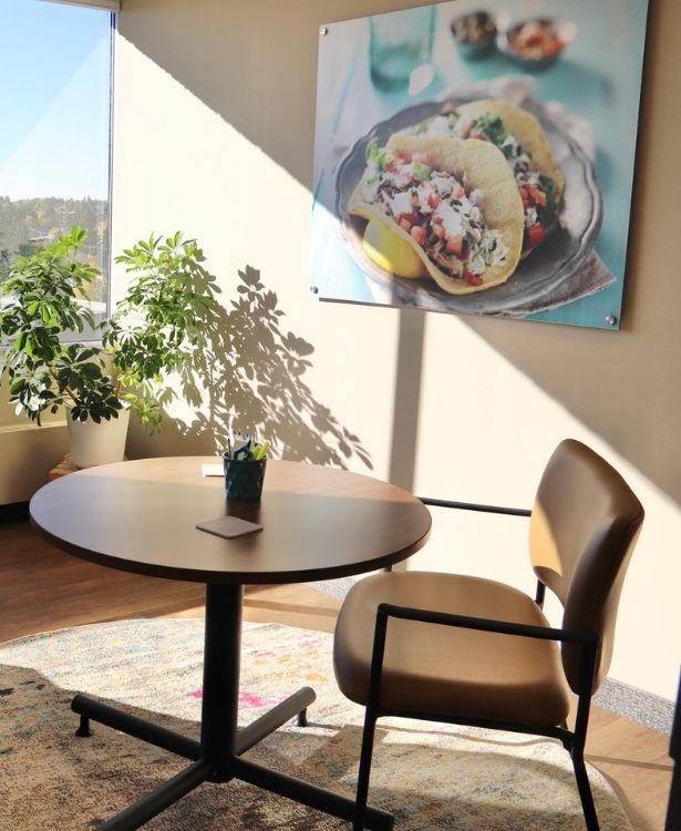 Calgary_Dietician_Office a chair with a round table on a carpet with a food image on the wall in a Calgary dietician's office