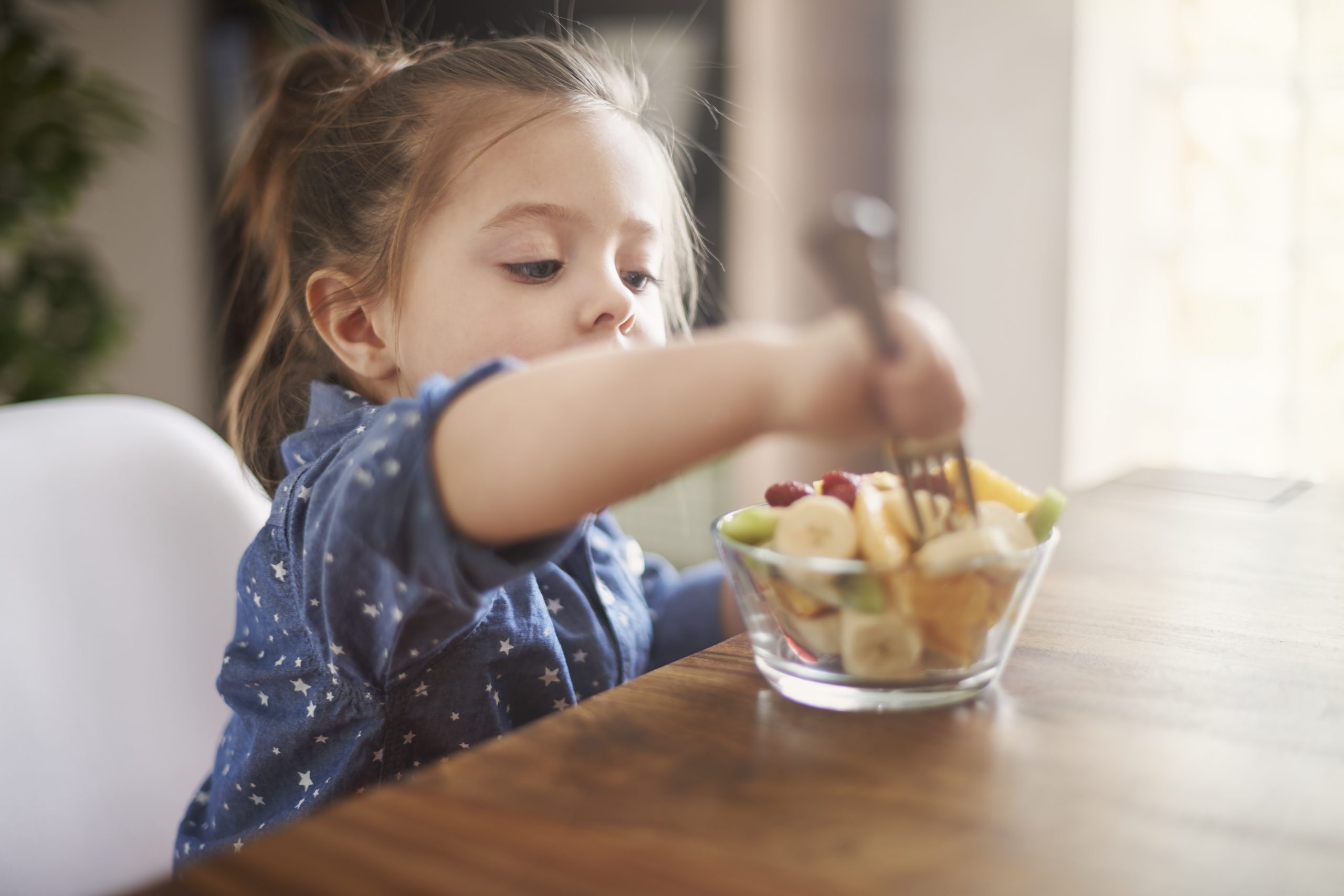 Child eating fruit out of a bowl with a fork.